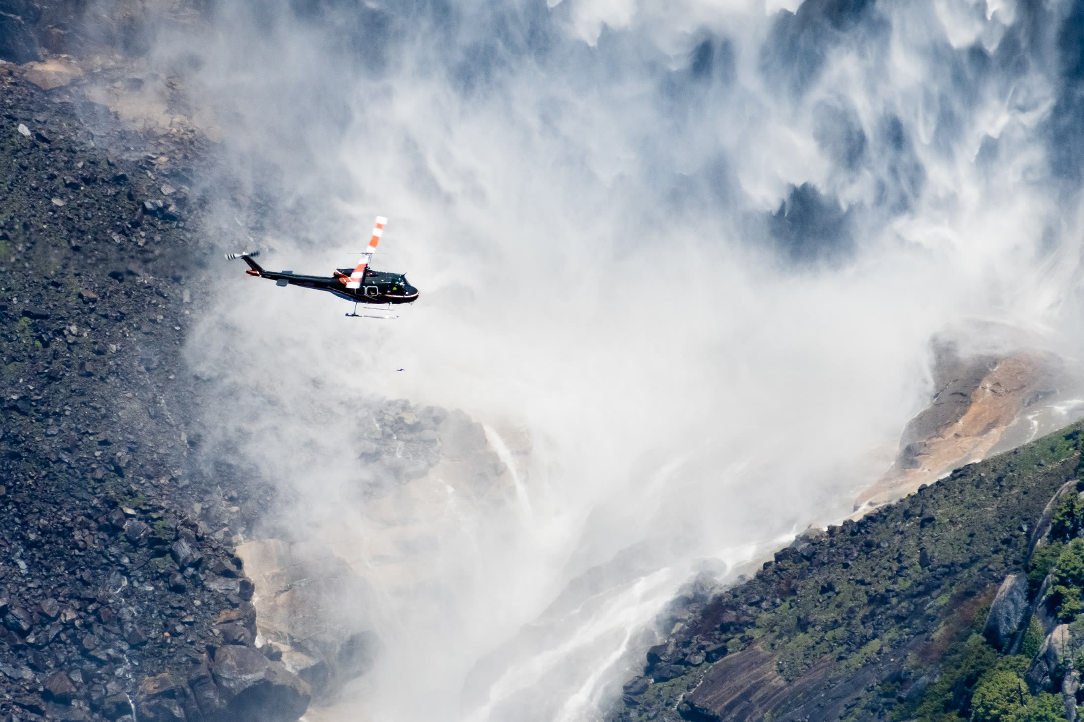 Utility helicopter operating over rugged mountain terrain in mist
